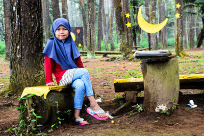 Full length of girl sitting on bench at forest