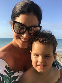 Portrait of smiling mother and son at beach against sky