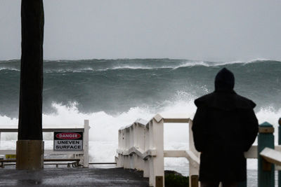 Rear view of person standing by railing against high tide
