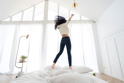 Full length rear view of young woman standing on bed