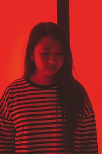 Young woman against illuminated red wall