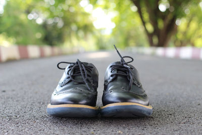 Close-up of shoes on road against trees