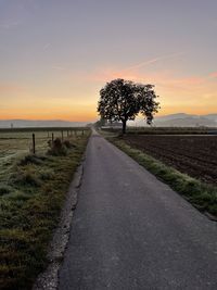 Road amidst field against sky during sunset