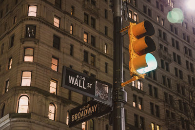 Low angle view of road sign against illuminated buildings in new york city.