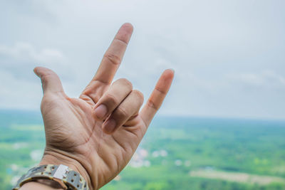 Cropped hand showing rock sign against sky