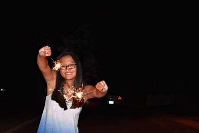 Portrait of happy woman holding sparklers during night