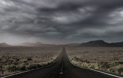 Empty long road amidst landscape against cloudy sky