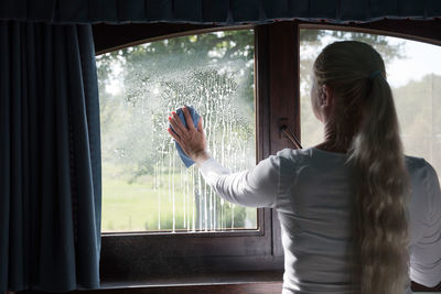 Woman cleaning window with special glass cleaner. look through soapy window