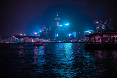 Illuminated buildings by sea against sky at night