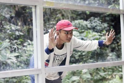 Boy looking through window against trees