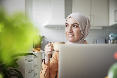 Smiling woman with hijab having coffee