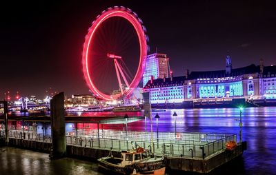 Illuminated ferris wheel by river against sky in city at night