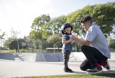 Side view of father assisting son in wearing helmet at skateboard park