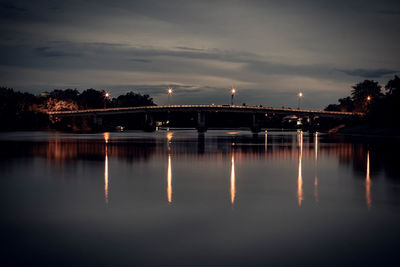 Illuminated bridge over river against sky at night