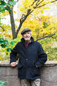 Portrait of confident senior man standing with hand in pocket in park during autumn