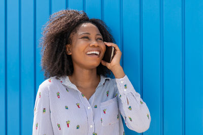 Smiling young woman looking away while standing against blue wall