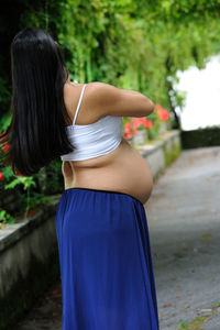 Beautiful hispanic woman expecting a baby, from behind walk in a public garden person