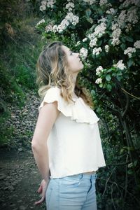 Side view of young woman looking at white flowers blooming outdoors