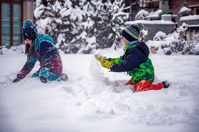 Full length of sibling playing with snow during winter