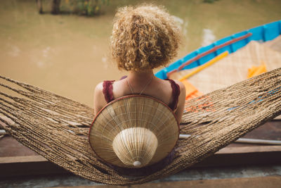 Rear view of woman sitting on hammock over river