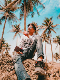 Full length of young man sitting on palm tree