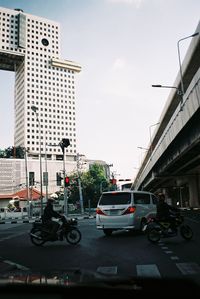 Vehicles on road by buildings in city against sky