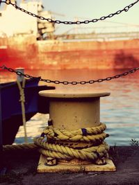 Close-up of rope tied to bollard at harbor against sky