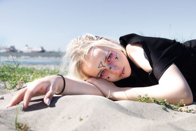 Portrait of young woman lying on beach against sky