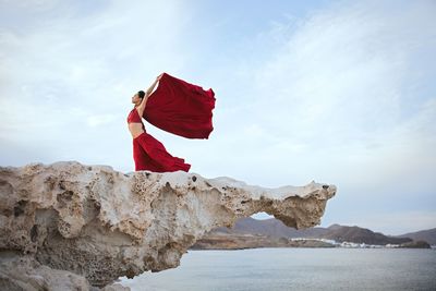 Man standing on rock by sea against sky