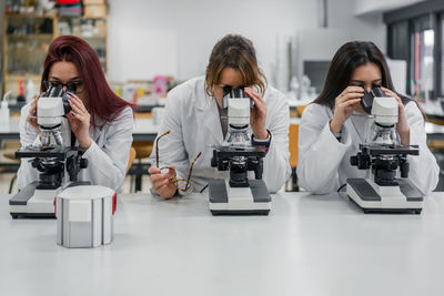 Women in white coats using modern microscopes to examine tissue cells during work in laboratory