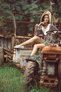 Young woman sitting on abandoned vehicle at field