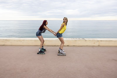 Friends roller skating and having fun at promenade by sea