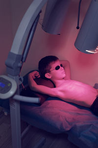 Boy lying under illuminated lighting equipment on bed