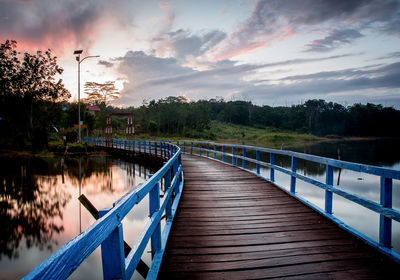 Footbridge over lake against sky during sunset