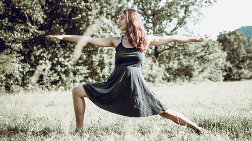 Beautiful young woman exercising on grassy field during sunny day