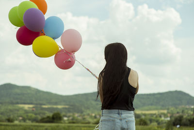 Rear view of woman with balloons standing against sky