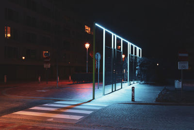 Illuminated street light on sidewalk by buildings in city at night