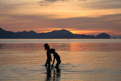 Silhouette men walking on beach against sky during sunset