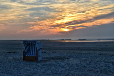 Hooded chair at beach against cloudy sky during sunset