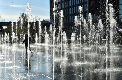 Fountain by lake against buildings in city