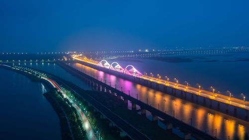 Illuminated bridge over river against sky at night