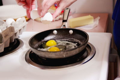 Cropped image of woman breaking egg on frying pan in kitchen