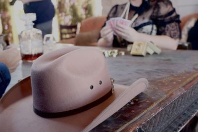 Close-up of cowboy western hat on table with hands holding cards and poker chips in the background 