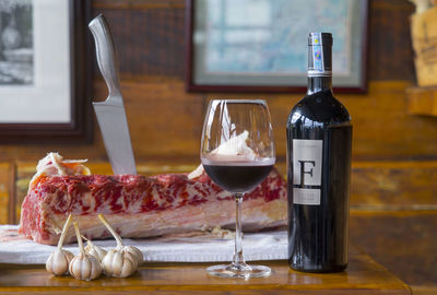 Knife in beef meat with vegetables and red wine on table