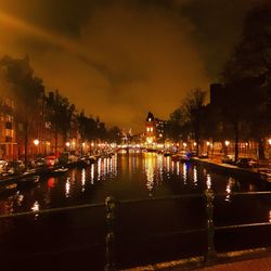 Illuminated city by river against sky at night