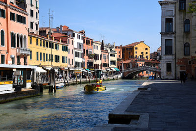 Canal by buildings in city against sky