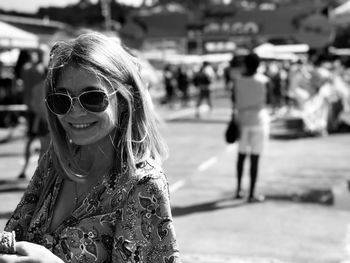 Portrait of young woman standing in city wearing sunglasses smiling while on her mobile phone