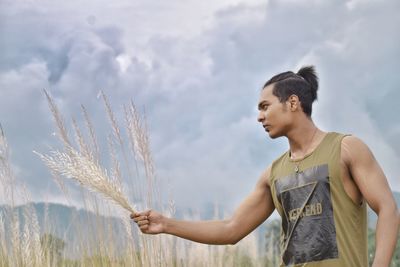 Young woman looking away against sky on field