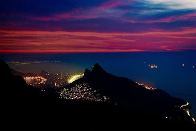 Scenic view of illuminated sea against dramatic sky at sunset