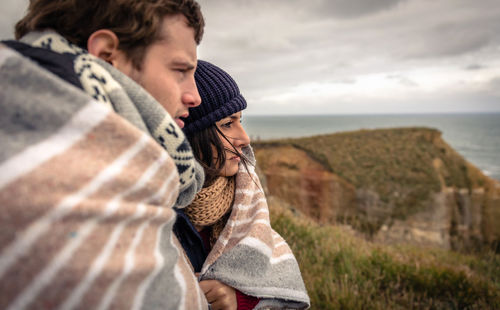 Couple covered with blanket looking at sea